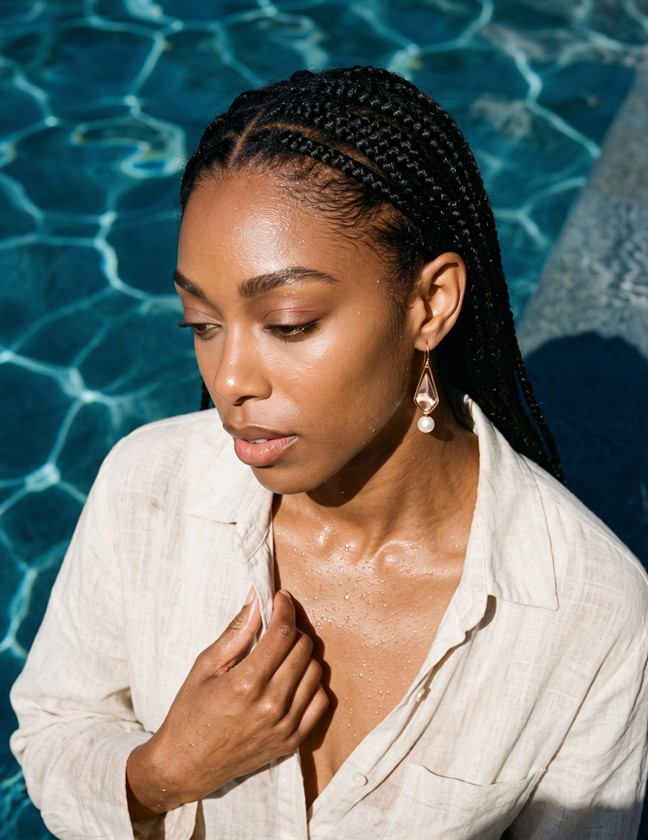 Model wearing pearl drop earrings beside a pool